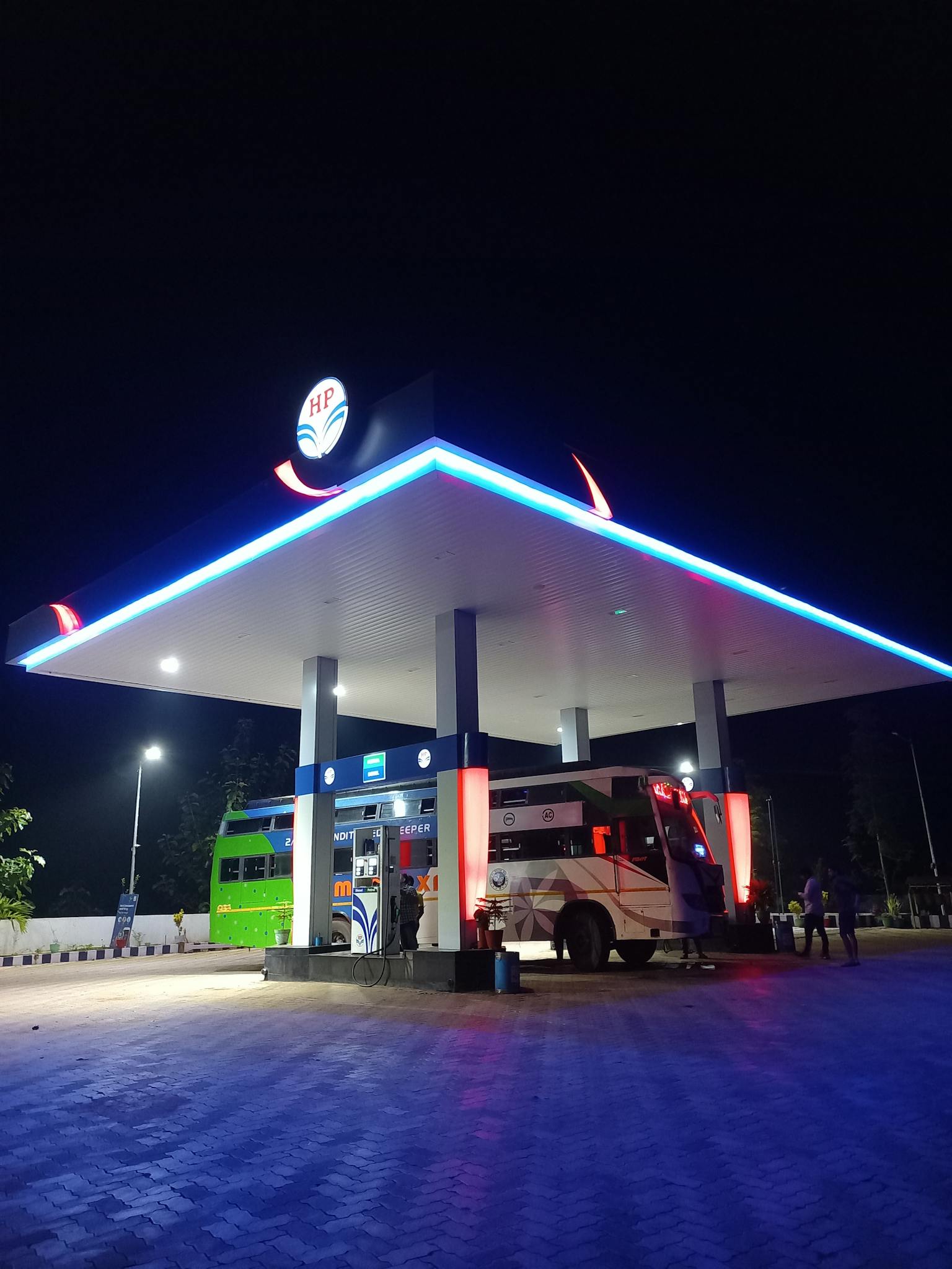 Illuminated gas station with buses parked at night in Bhubaneswar, India.